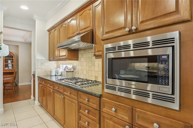 kitchen with decorative backsplash, light tile patterned floors, dark stone countertops, crown molding, and stainless steel appliances