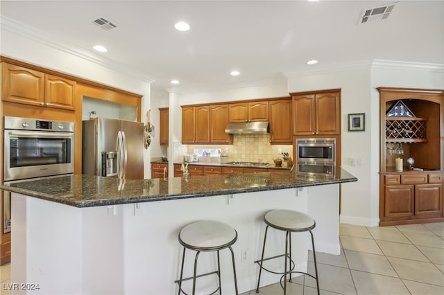 kitchen featuring a large island, light tile patterned floors, appliances with stainless steel finishes, a breakfast bar, and ornamental molding