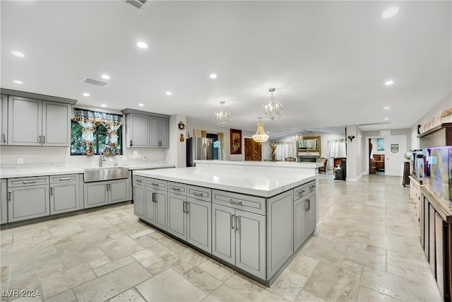 kitchen featuring a center island, hanging light fixtures, sink, gray cabinets, and stainless steel refrigerator