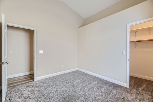 unfurnished bedroom featuring a spacious closet, vaulted ceiling, dark carpet, and a closet