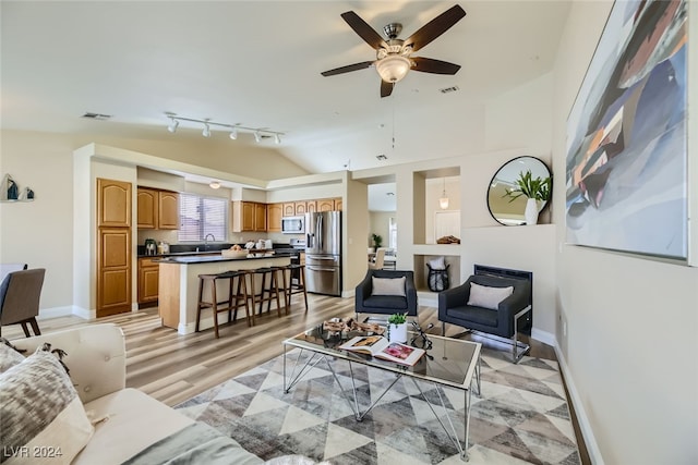 living room featuring sink, vaulted ceiling, light wood-type flooring, a fireplace, and ceiling fan