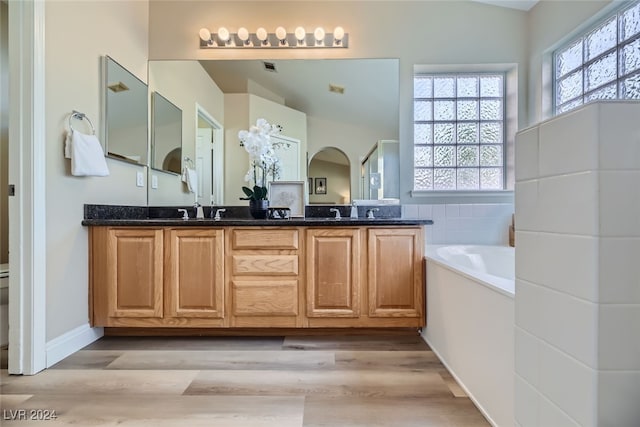 bathroom featuring vanity, lofted ceiling, a tub, and wood-type flooring