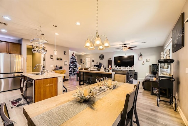 dining area with ceiling fan with notable chandelier, light hardwood / wood-style flooring, and sink