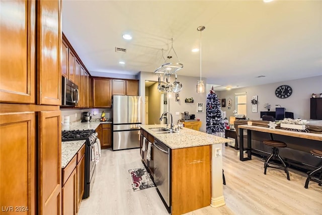 kitchen featuring a center island with sink, sink, light wood-type flooring, appliances with stainless steel finishes, and light stone counters