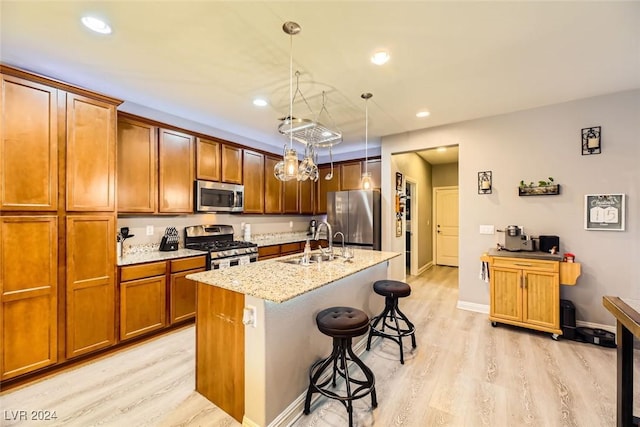 kitchen with appliances with stainless steel finishes, light wood-type flooring, a kitchen breakfast bar, sink, and hanging light fixtures