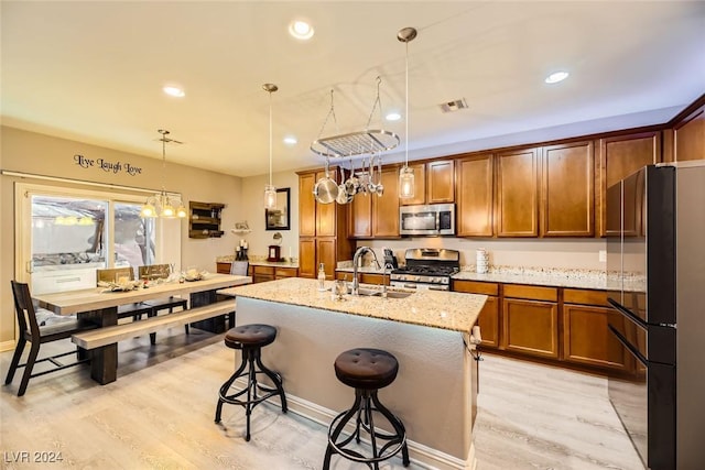 kitchen featuring stainless steel appliances, a center island with sink, hanging light fixtures, and light hardwood / wood-style floors