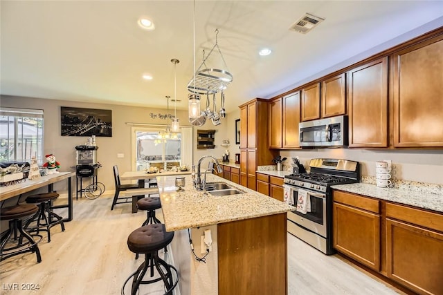 kitchen featuring light stone countertops, light wood-type flooring, stainless steel appliances, sink, and an island with sink