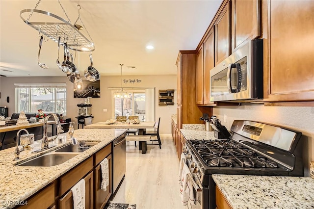 kitchen with light stone countertops, sink, hanging light fixtures, stainless steel appliances, and light hardwood / wood-style flooring