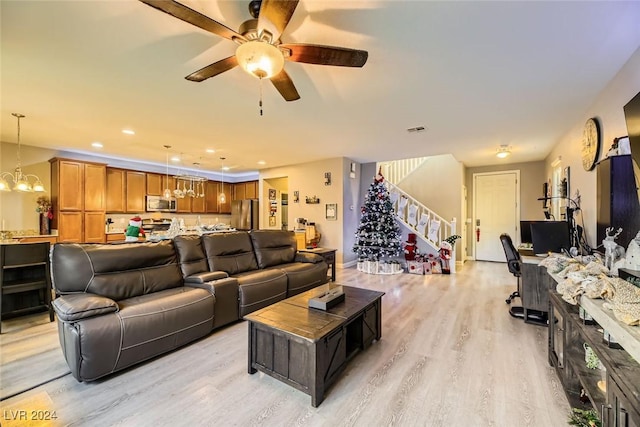 living room featuring ceiling fan with notable chandelier and light wood-type flooring