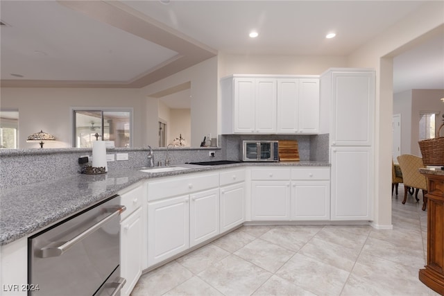 kitchen featuring tasteful backsplash, dishwasher, sink, stone countertops, and white cabinetry