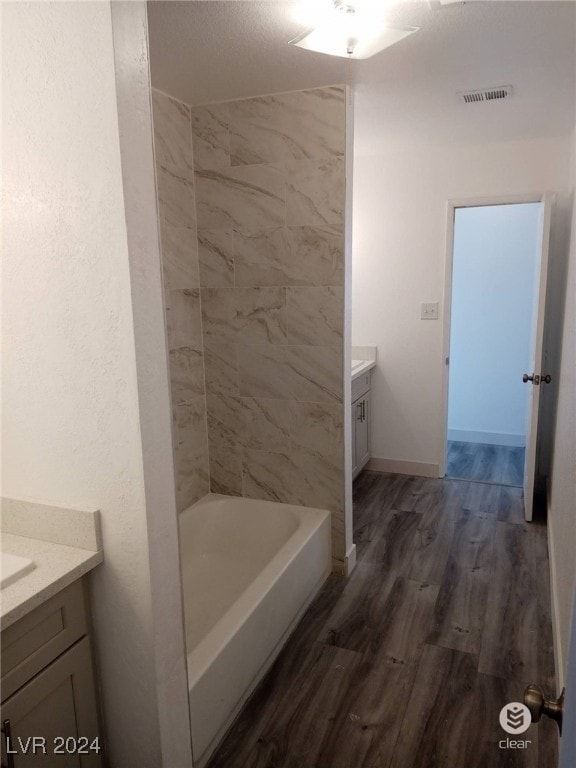 bathroom with hardwood / wood-style flooring, vanity, and tiled shower / bath