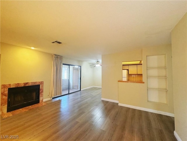 unfurnished living room featuring built in shelves, ceiling fan, a premium fireplace, and dark wood-type flooring