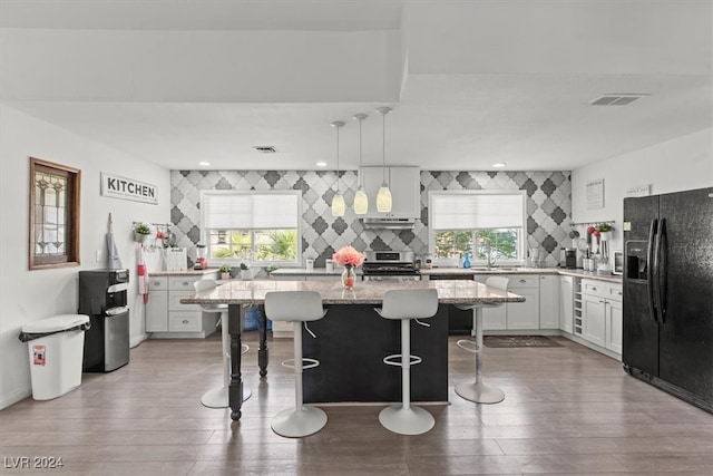 kitchen featuring a healthy amount of sunlight, black refrigerator with ice dispenser, decorative light fixtures, and a kitchen island