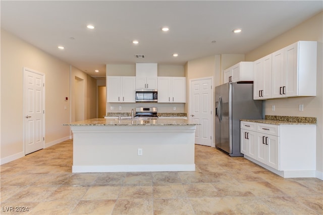 kitchen with stainless steel appliances, light stone countertops, white cabinets, and a kitchen island with sink