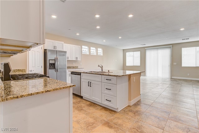 kitchen with stainless steel appliances, white cabinetry, light stone countertops, sink, and an island with sink