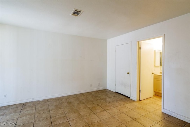 unfurnished bedroom featuring ensuite bathroom and light tile patterned floors