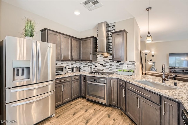 kitchen featuring wall chimney exhaust hood, stainless steel appliances, sink, light hardwood / wood-style floors, and hanging light fixtures