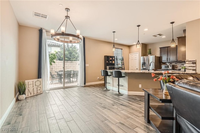 kitchen with stainless steel fridge, light stone counters, dark brown cabinets, light hardwood / wood-style floors, and a breakfast bar area