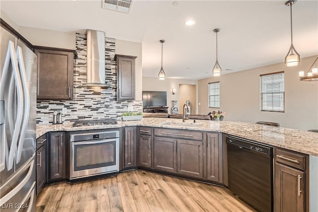 kitchen featuring wall chimney exhaust hood, light hardwood / wood-style floors, decorative light fixtures, and appliances with stainless steel finishes