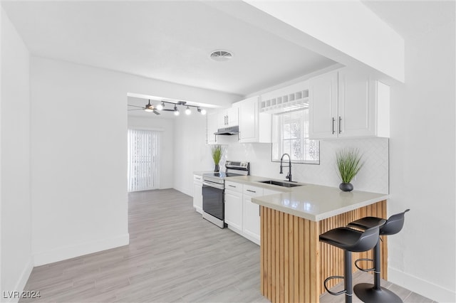 kitchen featuring stainless steel range with electric stovetop, light wood-type flooring, white cabinetry, sink, and a breakfast bar area