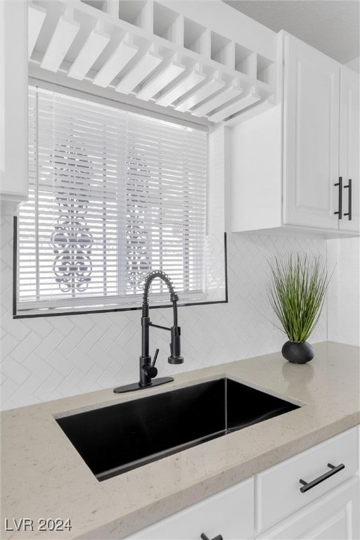 kitchen with tasteful backsplash, light stone countertops, sink, and white cabinets