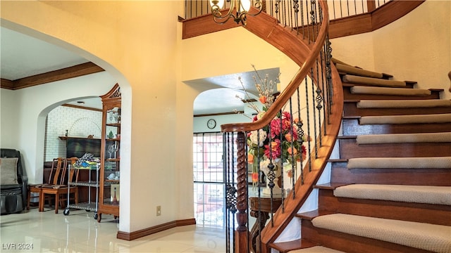 stairs featuring a towering ceiling, tile patterned floors, a chandelier, and crown molding