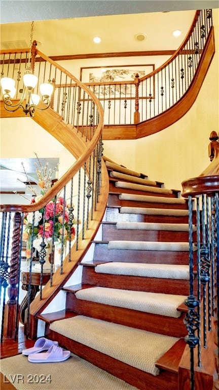 staircase with ornamental molding, hardwood / wood-style floors, and a notable chandelier