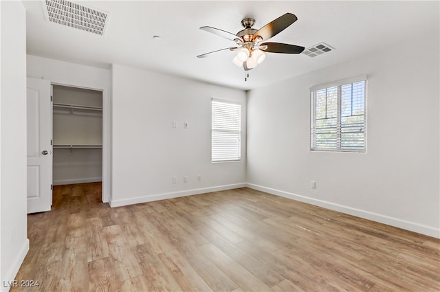 unfurnished bedroom with a closet, a walk in closet, ceiling fan, and light hardwood / wood-style flooring