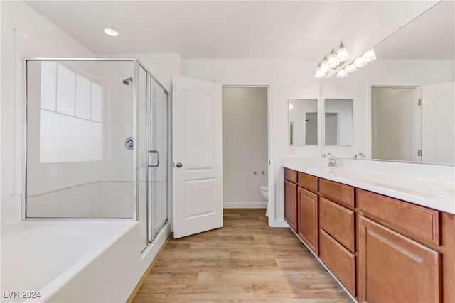 bathroom featuring toilet, a stall shower, wood finished floors, double vanity, and recessed lighting