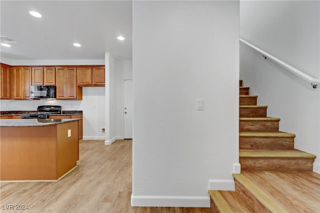 kitchen featuring light hardwood / wood-style floors, black appliances, and dark stone counters