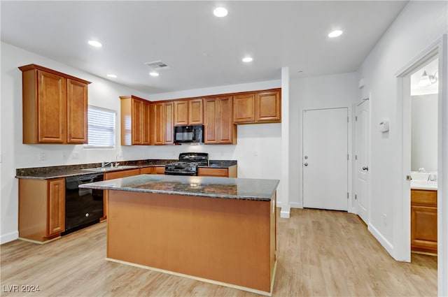 kitchen featuring dark stone counters, black appliances, sink, a kitchen island, and light hardwood / wood-style flooring