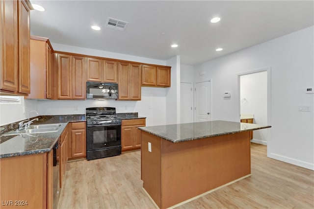 kitchen with light hardwood / wood-style floors, a center island, black appliances, sink, and dark stone countertops