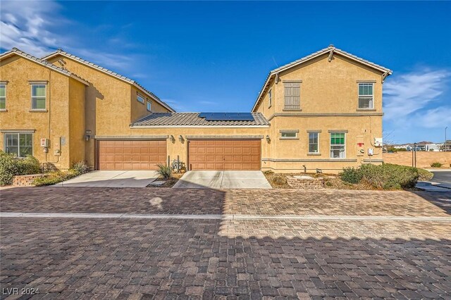 view of front of home with stucco siding, decorative driveway, roof mounted solar panels, and a tiled roof