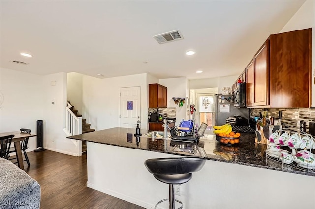 kitchen featuring visible vents, dark wood-type flooring, a peninsula, and decorative backsplash