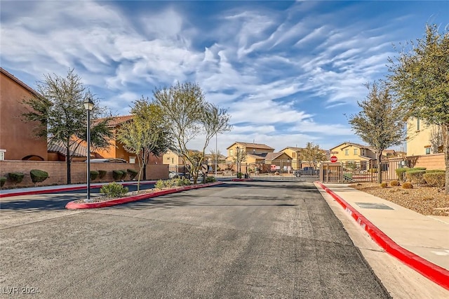 view of street featuring a gate, sidewalks, curbs, street lighting, and a residential view