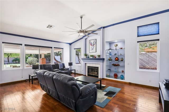 living room featuring a tiled fireplace, dark wood-type flooring, vaulted ceiling, ceiling fan, and built in features