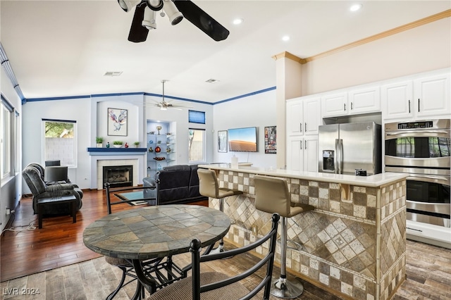 dining area featuring wood-type flooring, vaulted ceiling, ornamental molding, ceiling fan, and a fireplace