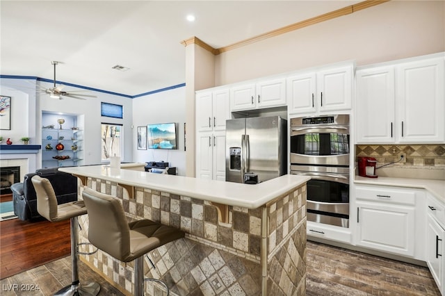 kitchen with white cabinets, a kitchen breakfast bar, appliances with stainless steel finishes, and dark wood-type flooring