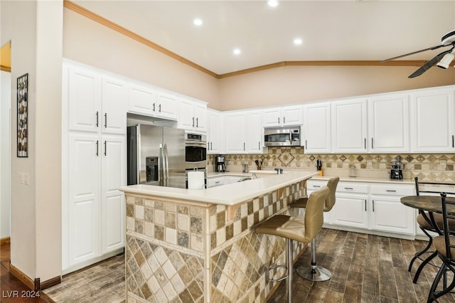 kitchen with a center island with sink, vaulted ceiling, a breakfast bar, white cabinetry, and appliances with stainless steel finishes