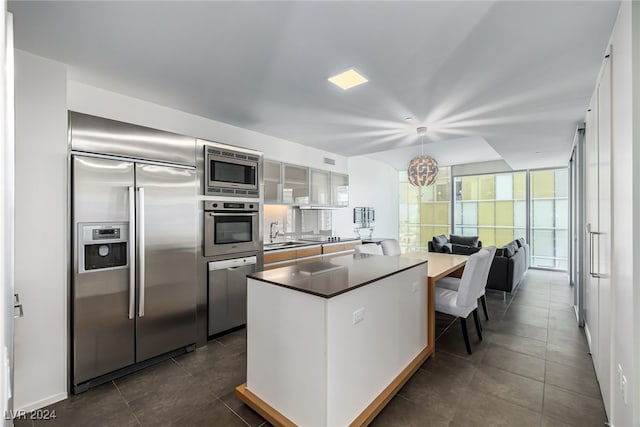 kitchen featuring built in appliances, white cabinetry, sink, a notable chandelier, and dark tile patterned flooring