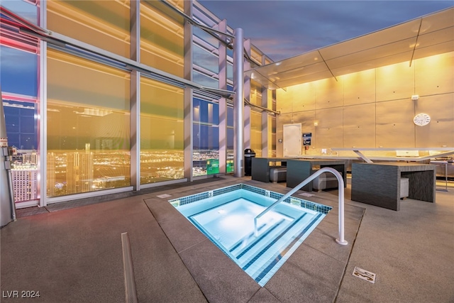 pool at dusk with a hot tub and a patio