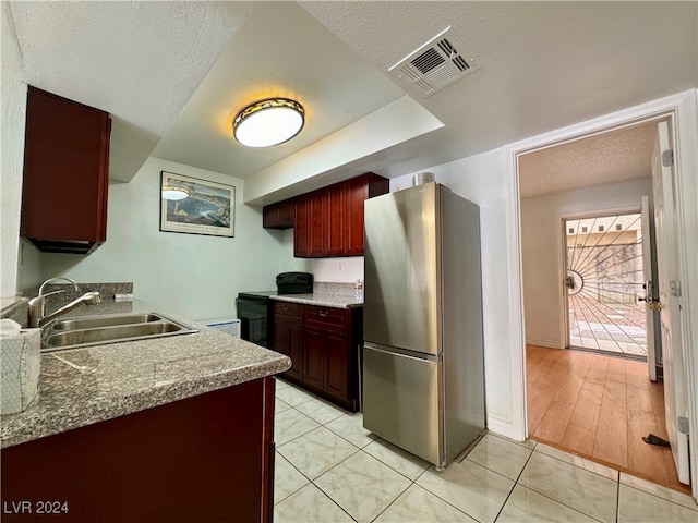 kitchen with a textured ceiling, sink, black range with electric stovetop, stainless steel refrigerator, and light hardwood / wood-style flooring