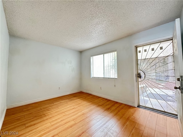 empty room with a textured ceiling and light hardwood / wood-style flooring