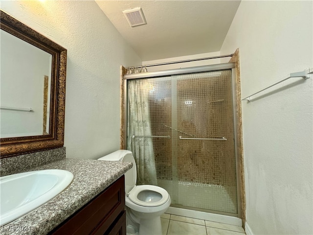 bathroom with a shower with door, vanity, a textured ceiling, tile patterned flooring, and toilet