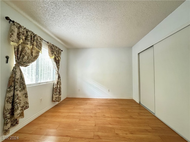 unfurnished bedroom featuring light hardwood / wood-style floors, a textured ceiling, and a closet