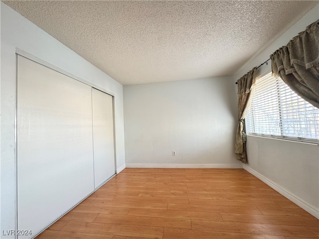 unfurnished bedroom with light hardwood / wood-style floors, a textured ceiling, and a closet