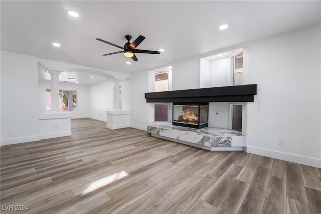 unfurnished living room with decorative columns, a multi sided fireplace, ceiling fan, and light hardwood / wood-style floors