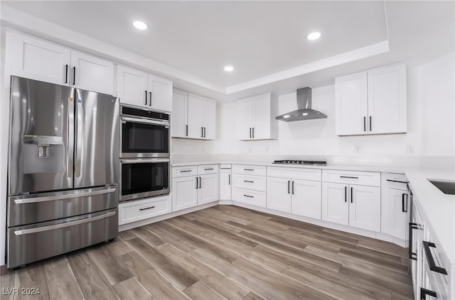 kitchen featuring white cabinetry, wall chimney range hood, and stainless steel appliances