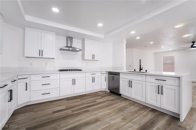 kitchen featuring dishwasher, kitchen peninsula, wall chimney exhaust hood, white cabinets, and sink