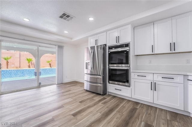 kitchen featuring stainless steel appliances, light hardwood / wood-style floors, white cabinets, and a textured ceiling